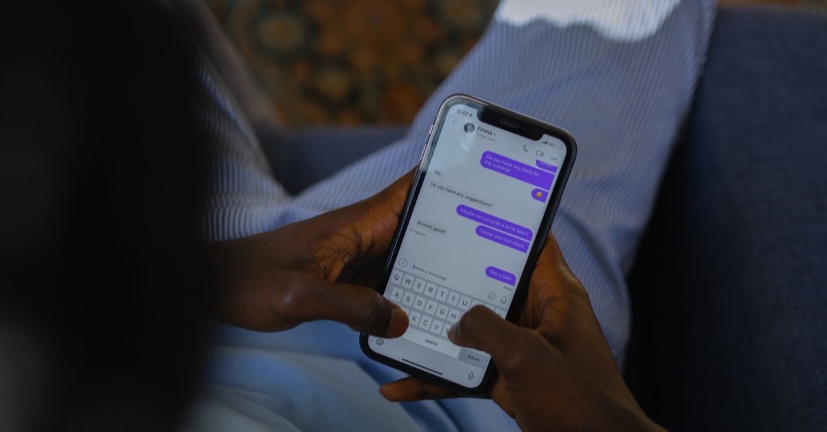Person holding a smartphone in both hands, typing a reply in an open text message conversation