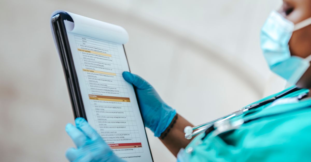 Clinician in teal scrubs and blue gloves holding a clipboard and reading a printed checklist form
