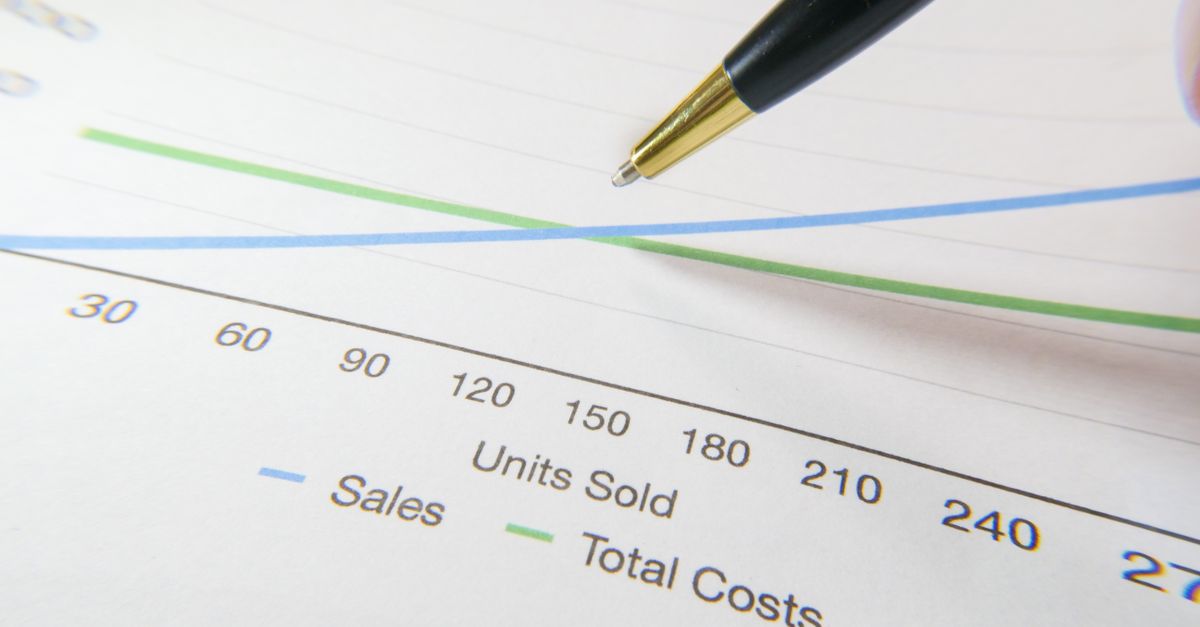 Pen pointing at a printed line graph comparing sales against total costs across units sold