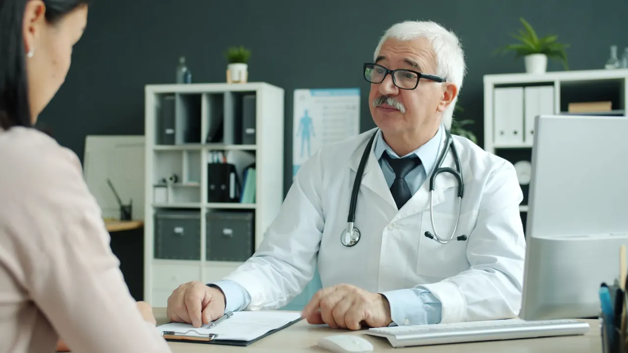 Experienced physician in conversation with a returning patient in a consulting room