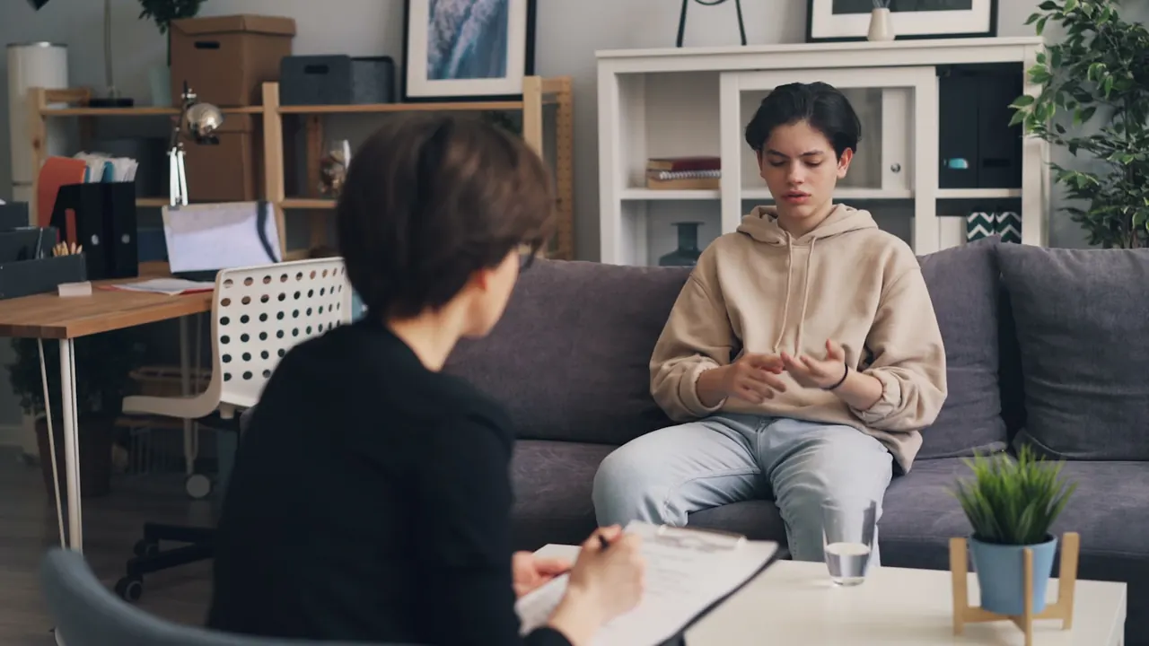 Counselor with a clipboard listening to a client seated on a couch in a therapy practice office